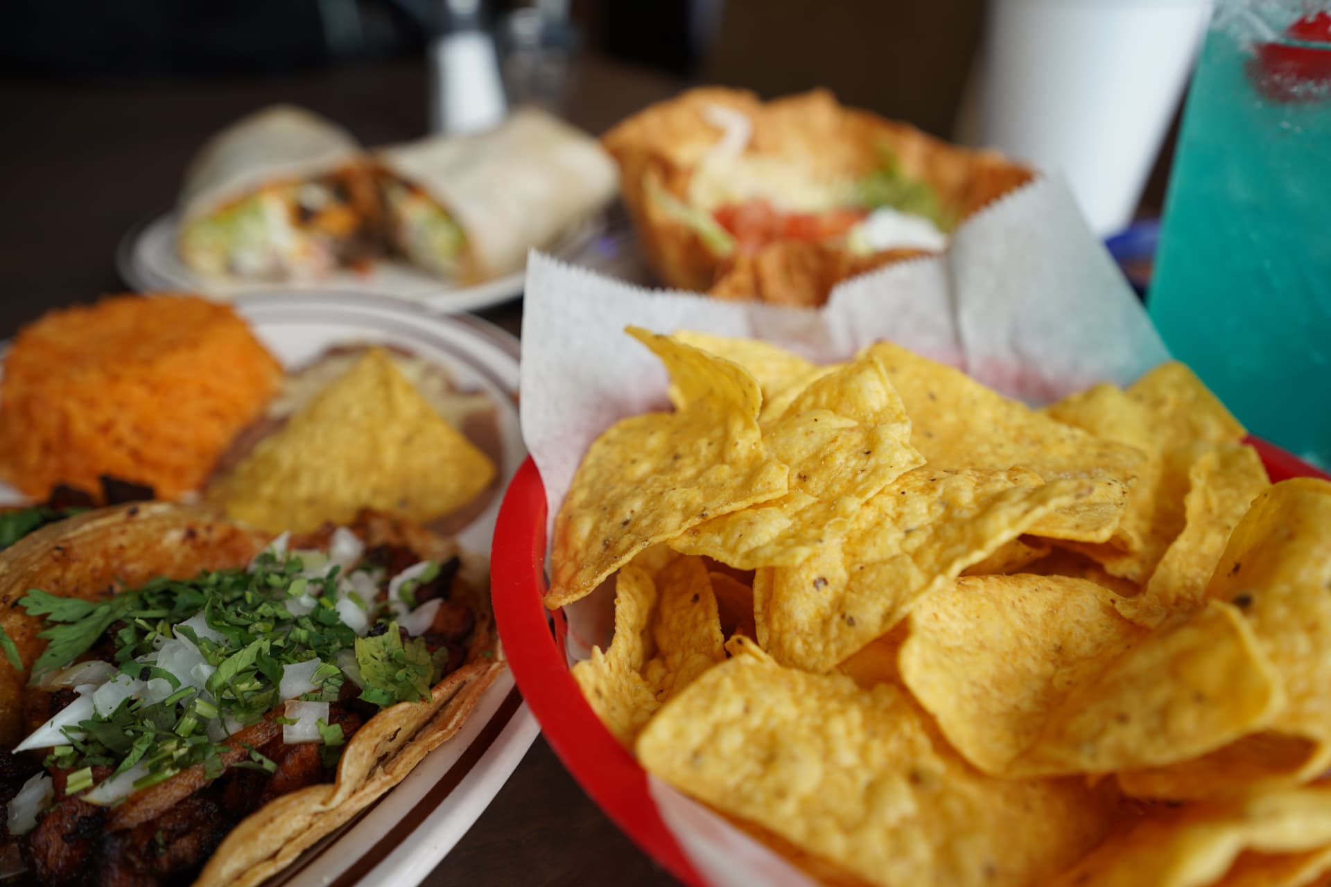 Fresh tortilla chips beside tacos, rice, burrito, chilaquiles, and a blue drink
