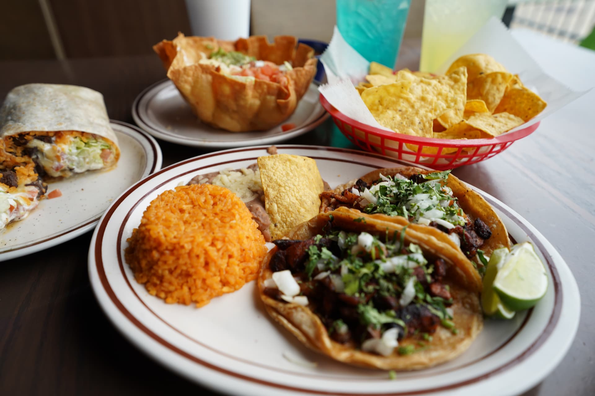 Carne asada taco dinner with rice, beans, chips, salad, burrito, and drinks