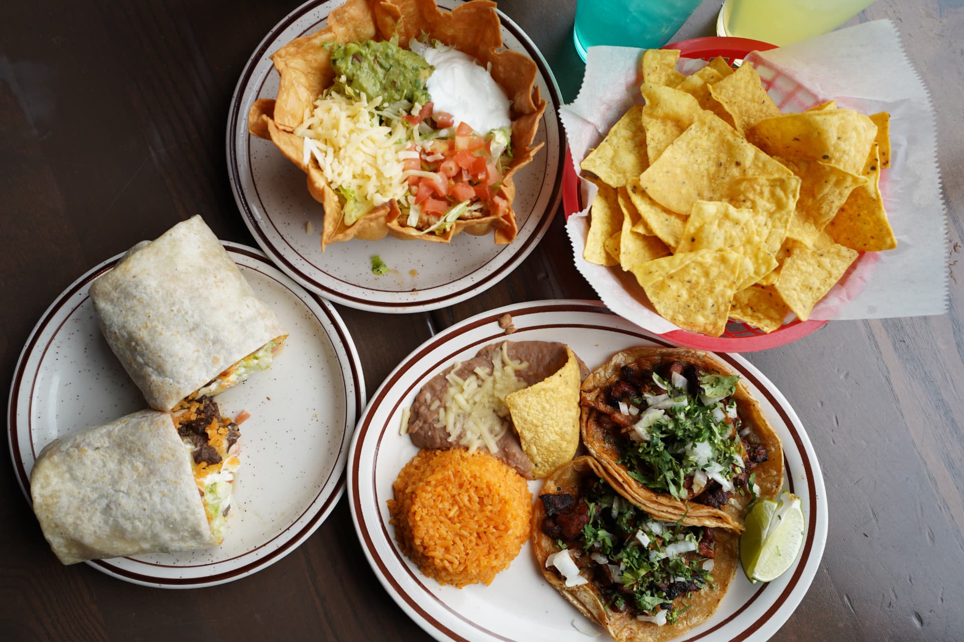 Overhead spread of tacos, burrito, taco salad, chips, and drinks